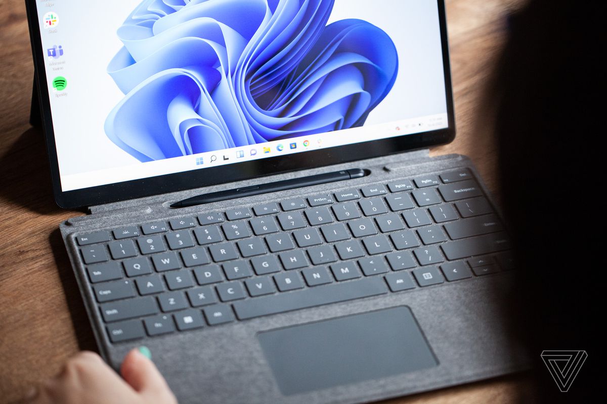 The Surface Pro 8 open, up close, with the keyboard pulled out and the stylus visible. The screen displays a blue swirl on a white background.