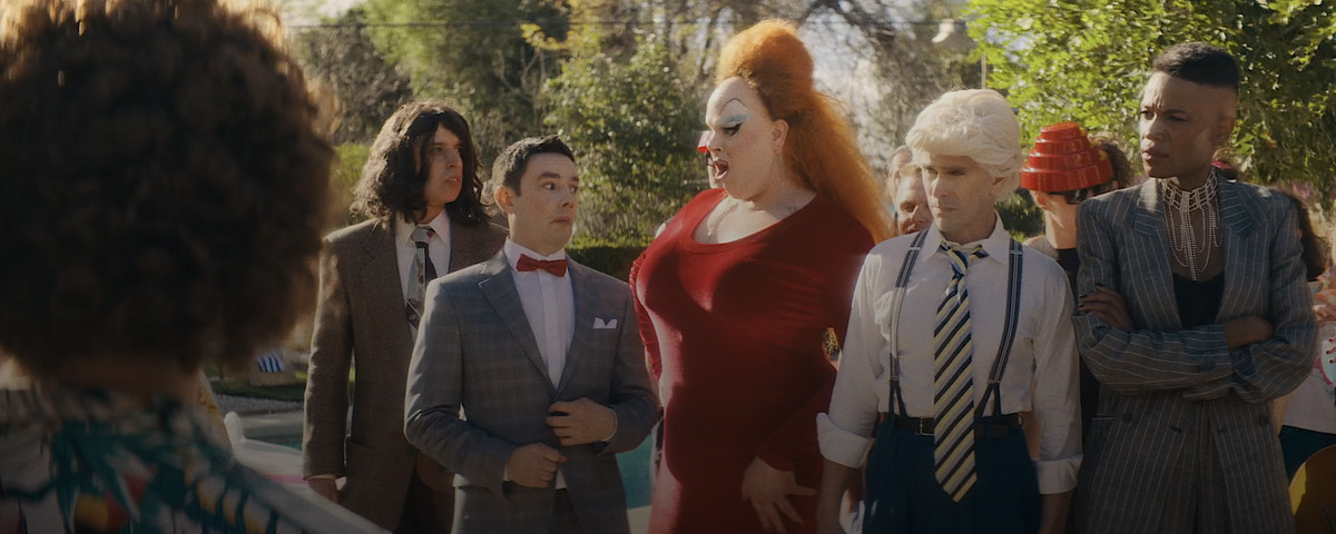 “Weird Al” Yankovic (Daniel Radcliffe, seen from behind) faces a series of other ’80s celebrities, including Tiny Tim (Demetri Martin), Pee-wee Herman (Jorma Taccone), and Divine (Nina West), in Weird: The Al Yankovic Story