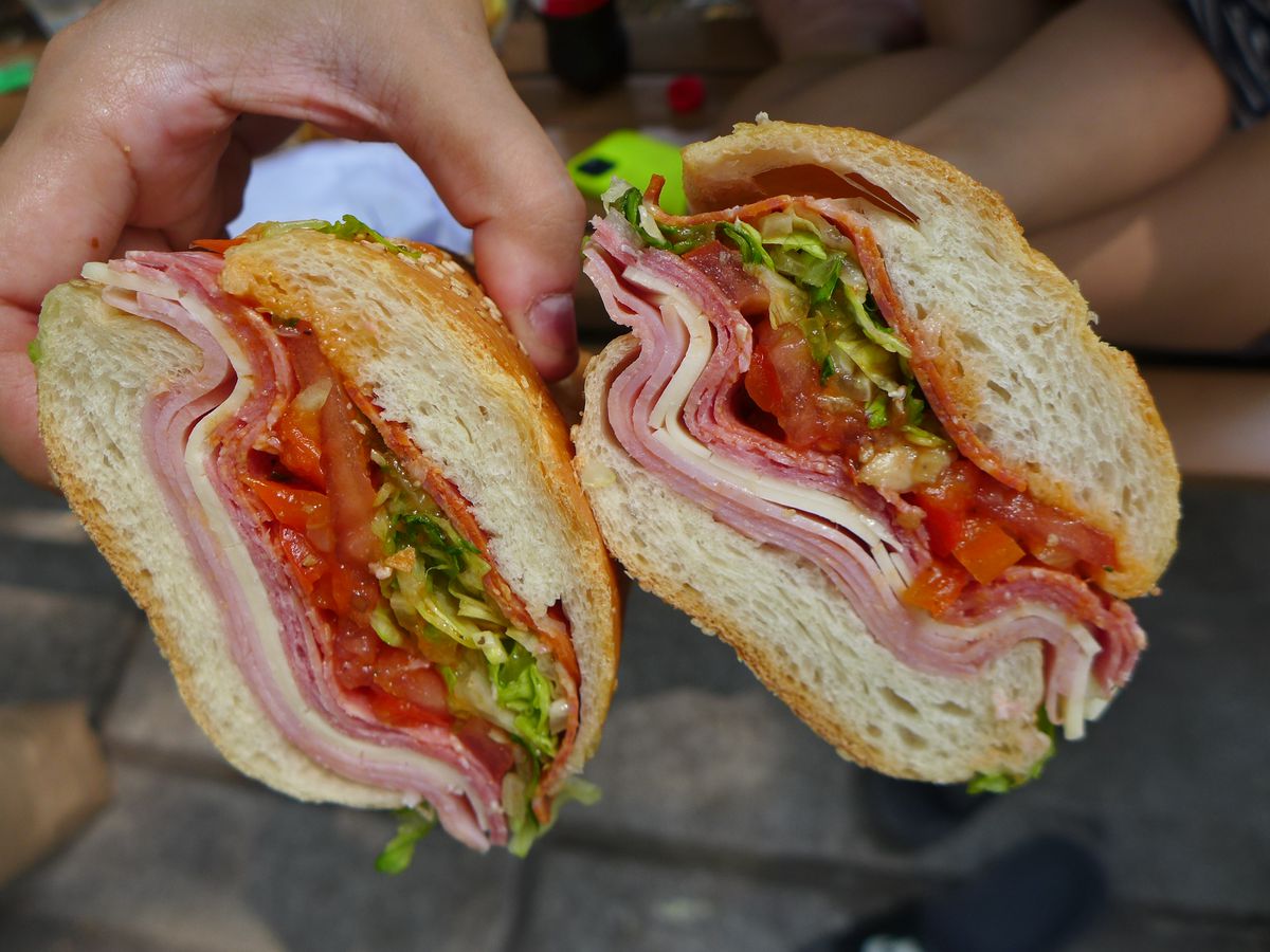 Two sandwich halves held aloft with cold cuts and cheese visible.