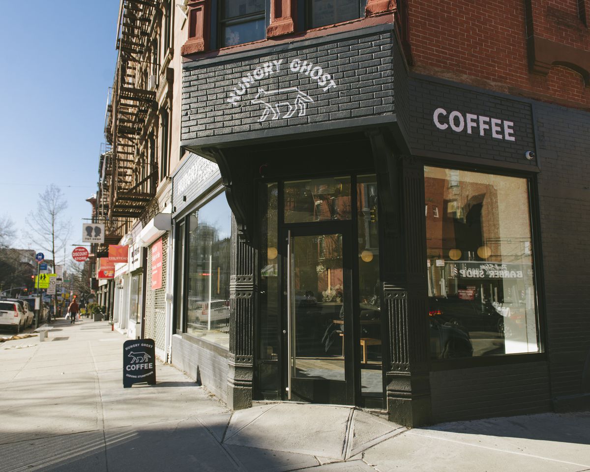 The exterior of a coffee shop with brick painted in black and a glass door entrance