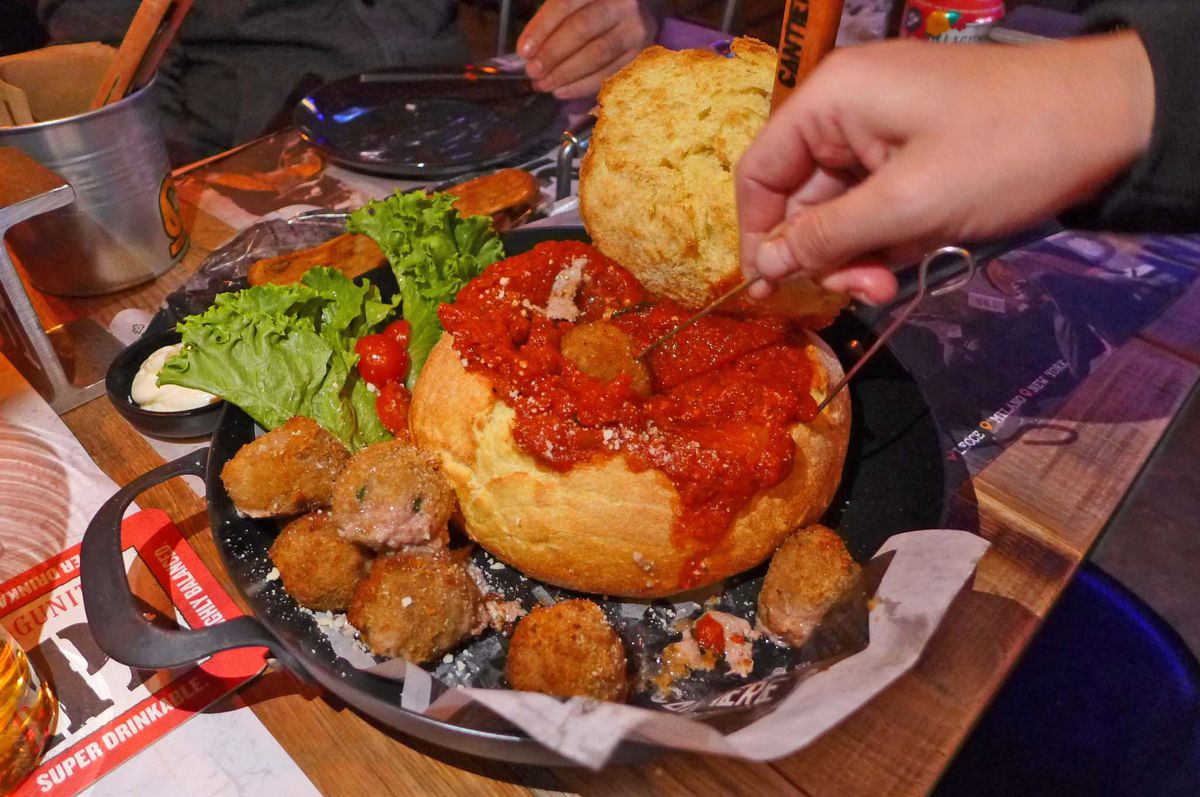 A round loaf of bread filled with marinara and surrounded by meatballs for dipping.