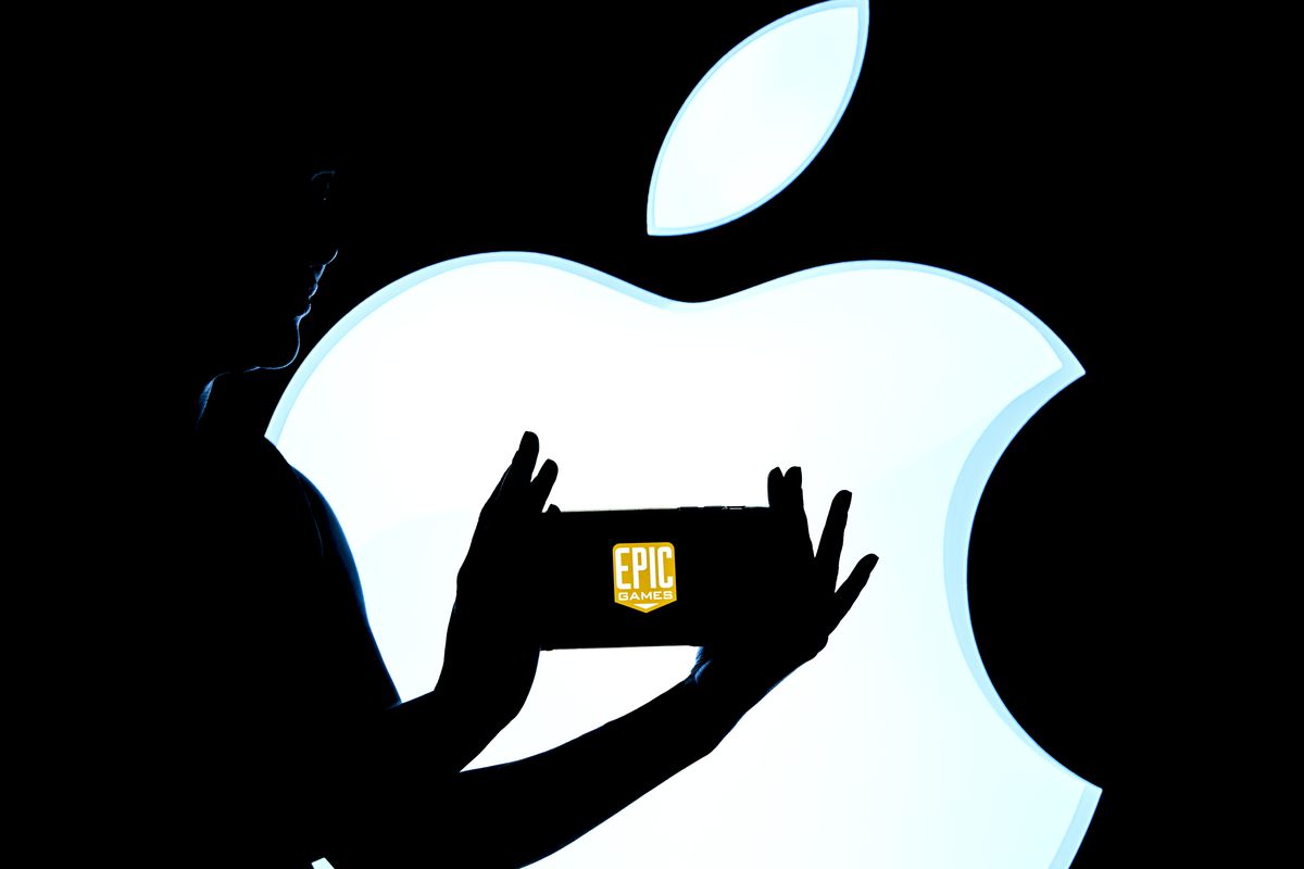 An image of the Epic Games logo on a phone being held up in front of a giant Apple logo