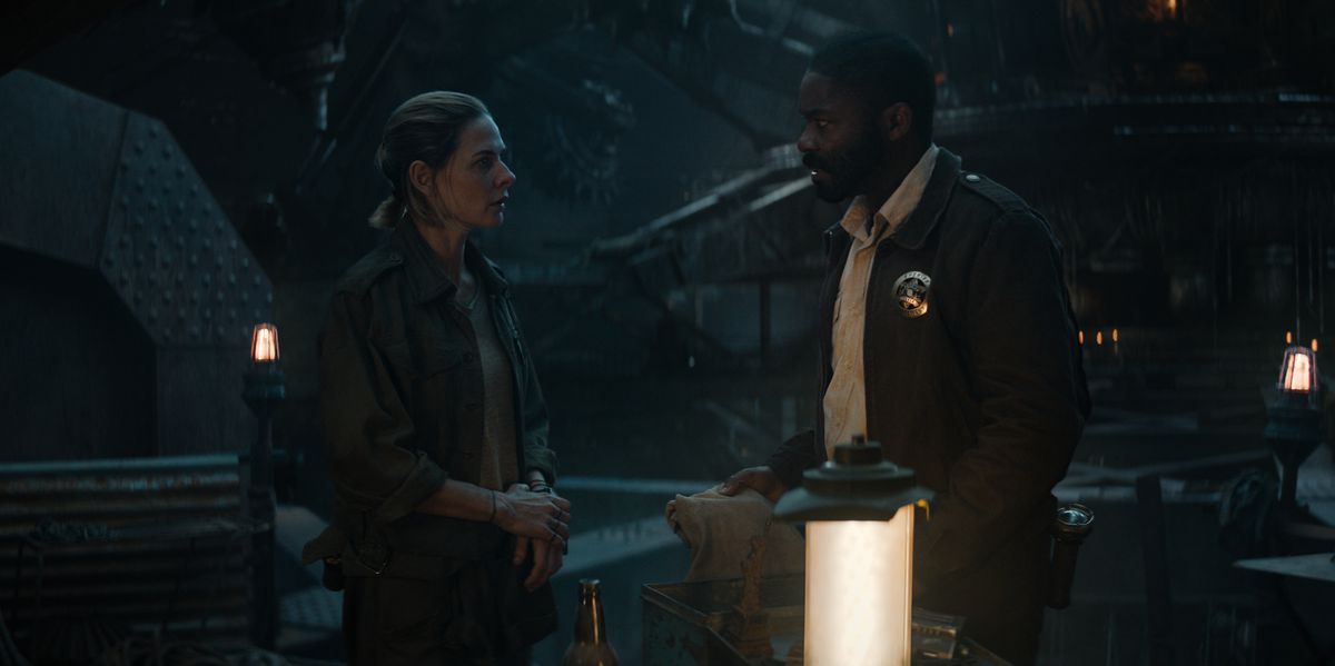 A woman (Rebecca Ferguson) stands across from a man (David Oyelowo) wearing a sheriff’s badge in a dark industrial setting flanked by futuristic lanterns.