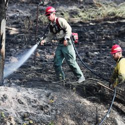 Two firefighters put water on a burning pole after extinguishing a brush fire along the eastbound lanes of I-80 east of Tooele on Sunday, July 7, 2019. The fire caused long traffic delays Sunday afternoon.