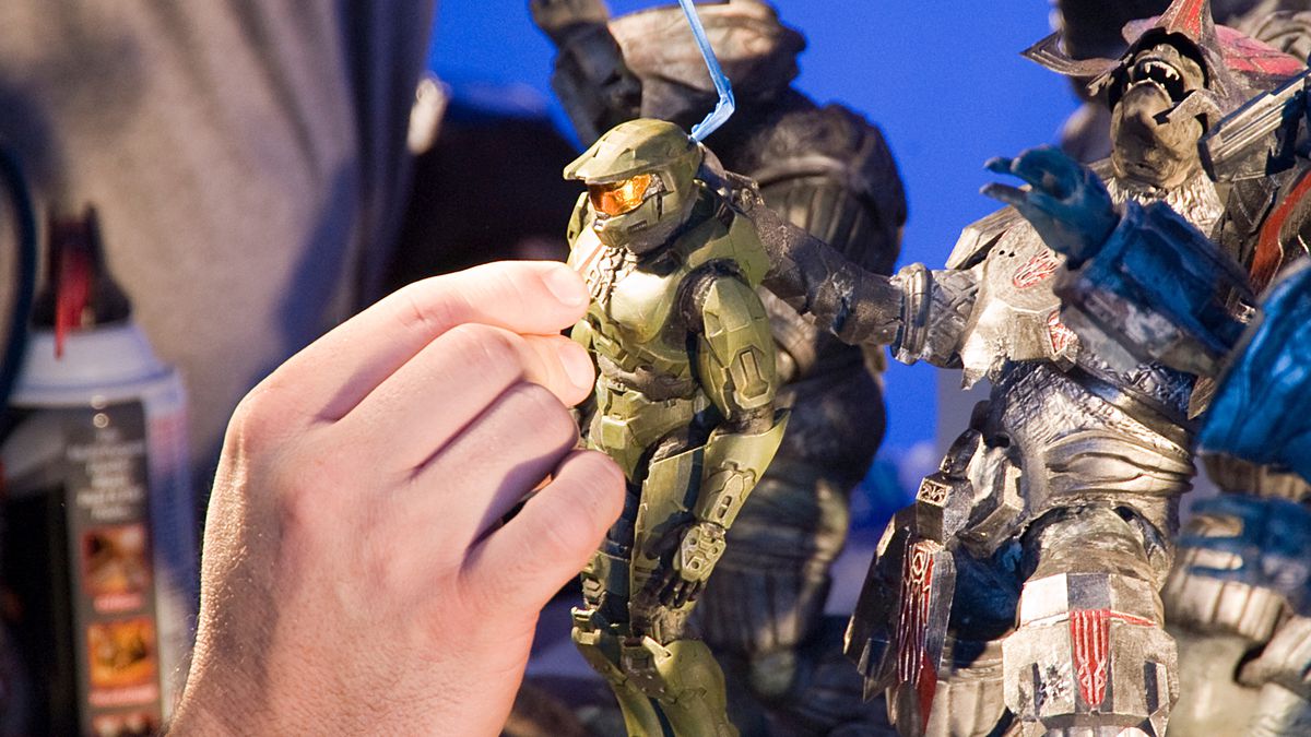 A human hand reaches into the “Halo 3: Believe” diorama to place the body of Master Chief.