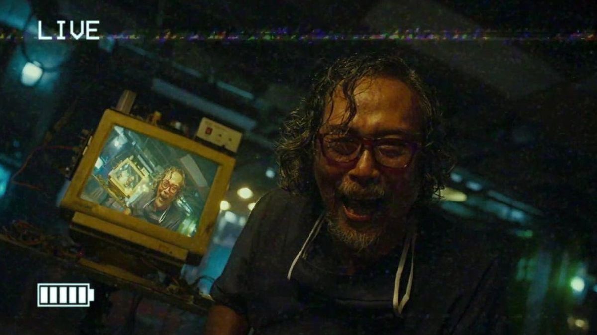 A crazed man laughs maniacally into a video camera starring at a recursive image of himself seen on a nearby monitor in VHS ’94.