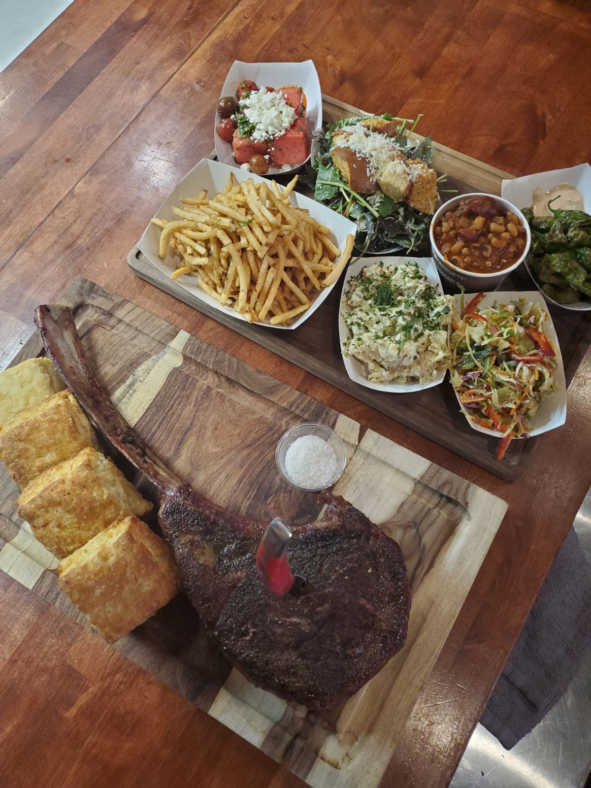 A tomahawk steak with several barbecue-style sides and four biscuits.
