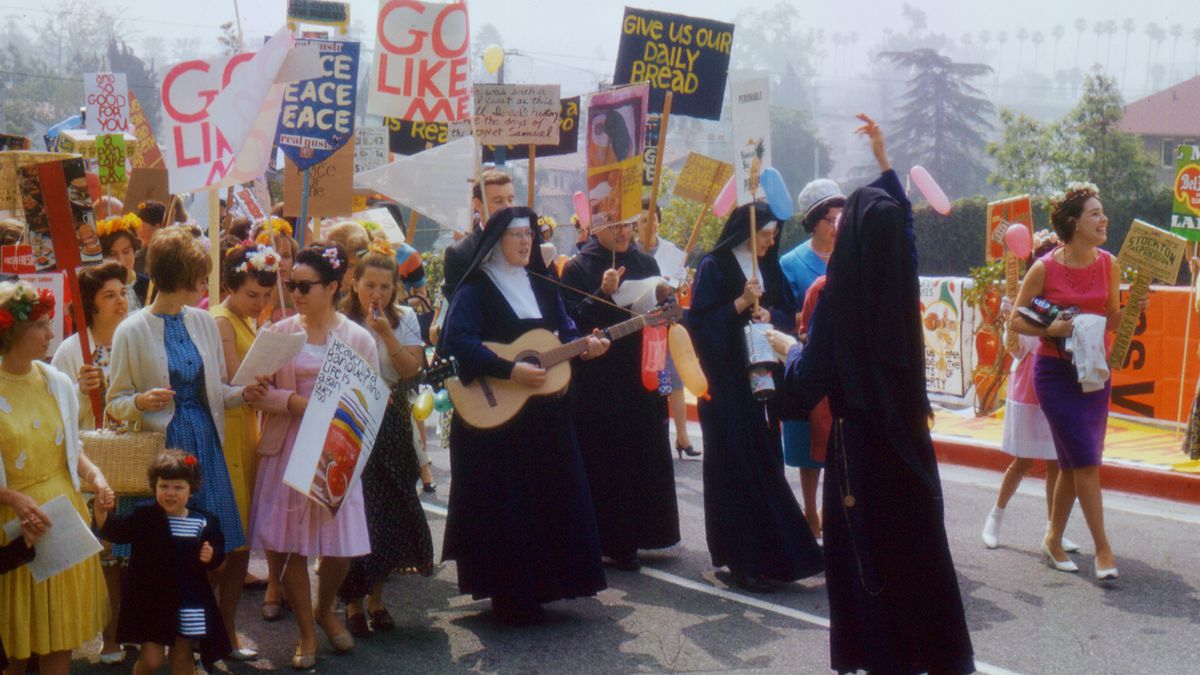 A group of nuns leads a crowd of sign-holding protestors, mostly women.