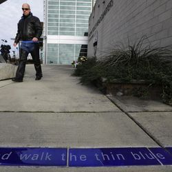Nathan Kile, who works as a corrections officer, walks near tiles that read "And walk the thin blue line," as he visits a growing memorial outside the Tacoma Police Department headquarters Thursday, Dec. 1, 2016, in Tacoma, Wash. A Tacoma Police officer died Wednesday night at a hospital after being shot multiple times earlier in the day while answering a domestic violence call. 