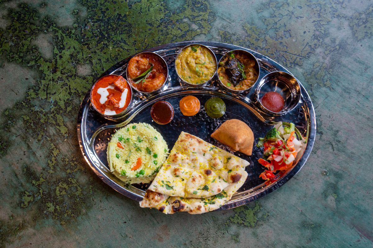 A thali with naan, rice, and a variety of small bowls filled with sauces and vegetables.
