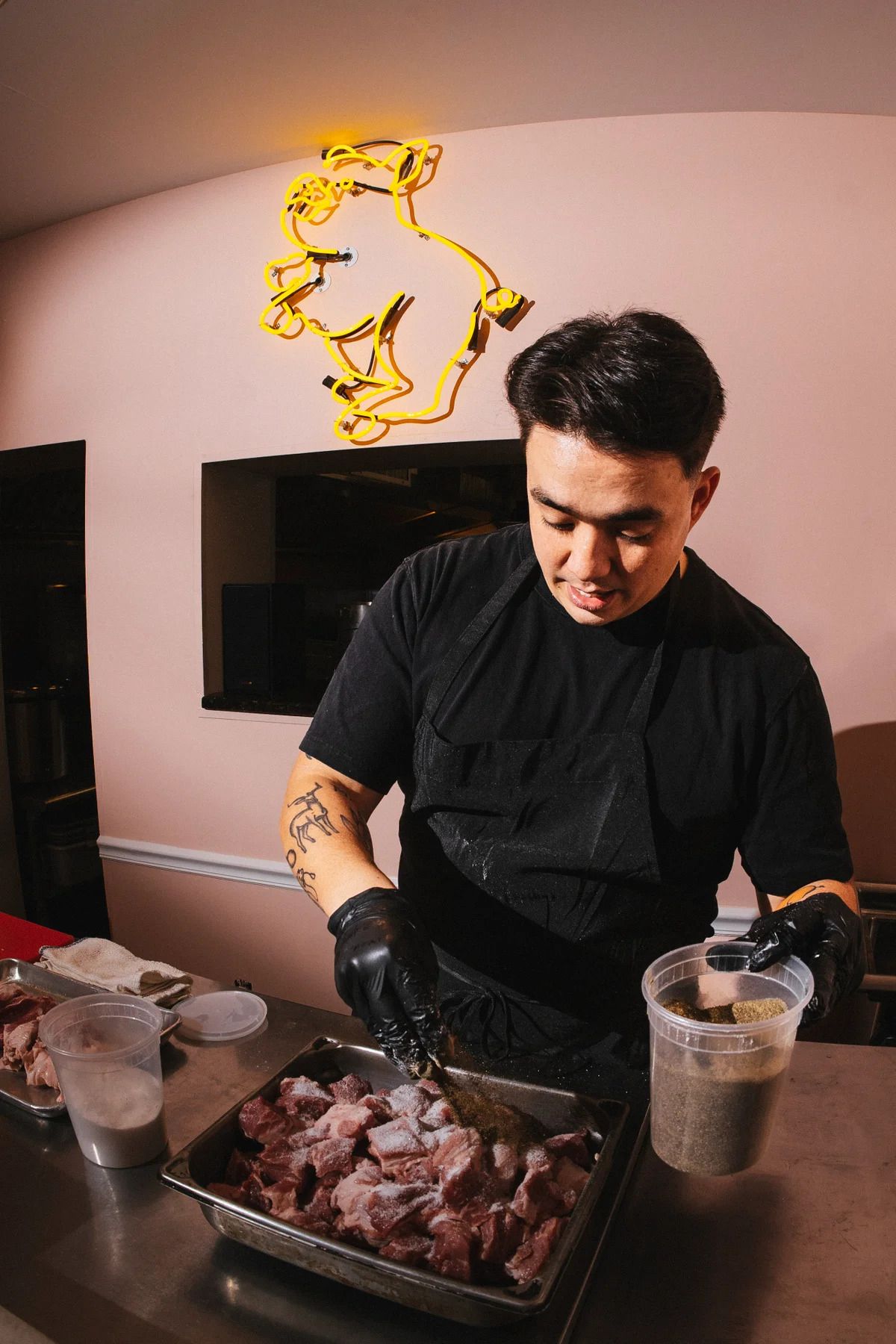 An Asian male chef preparing ribs in a container wearing black latex gloves. 