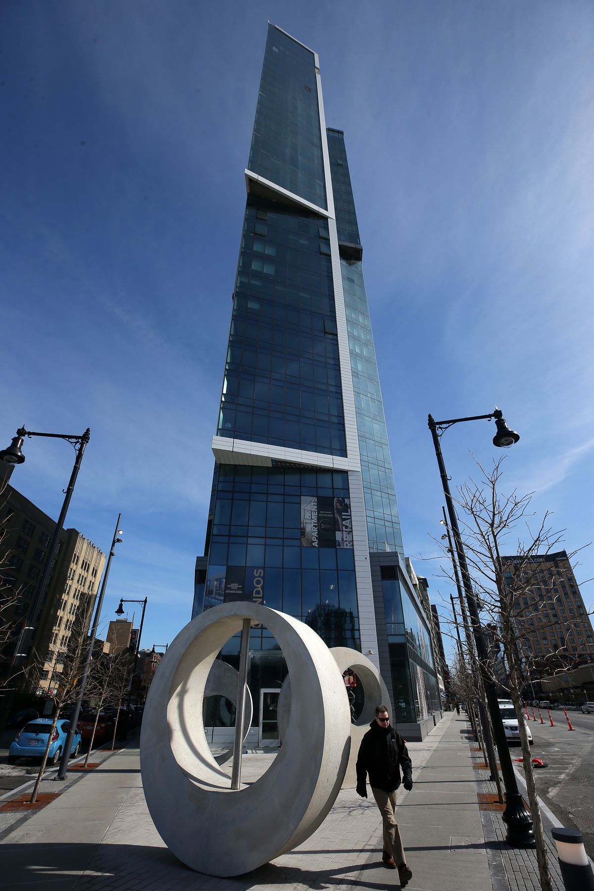 A boxy, triangular, glassy tower rising from a sidewalk. 