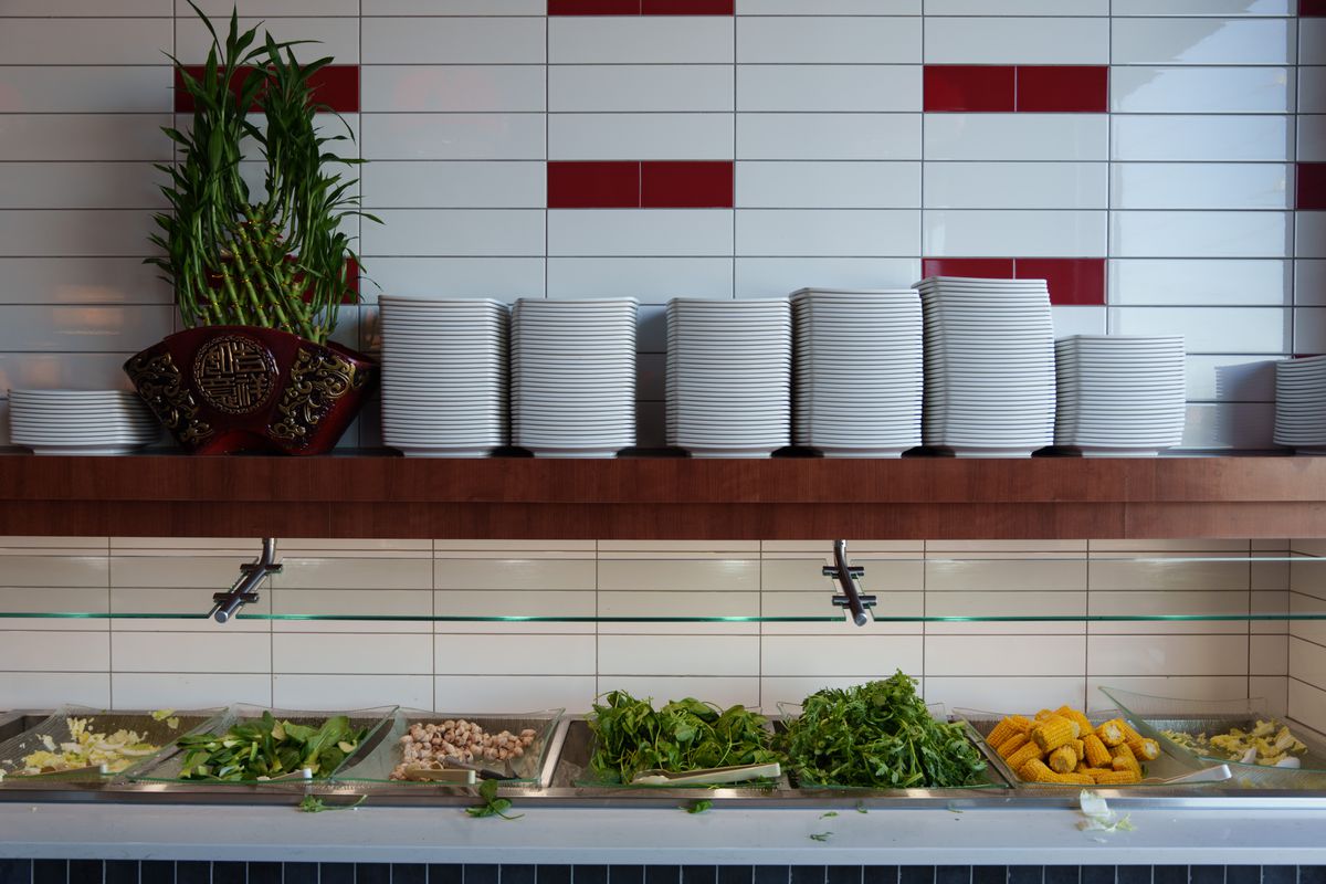 A buffet of fresh vegetables with a shelf covered in white plates. 