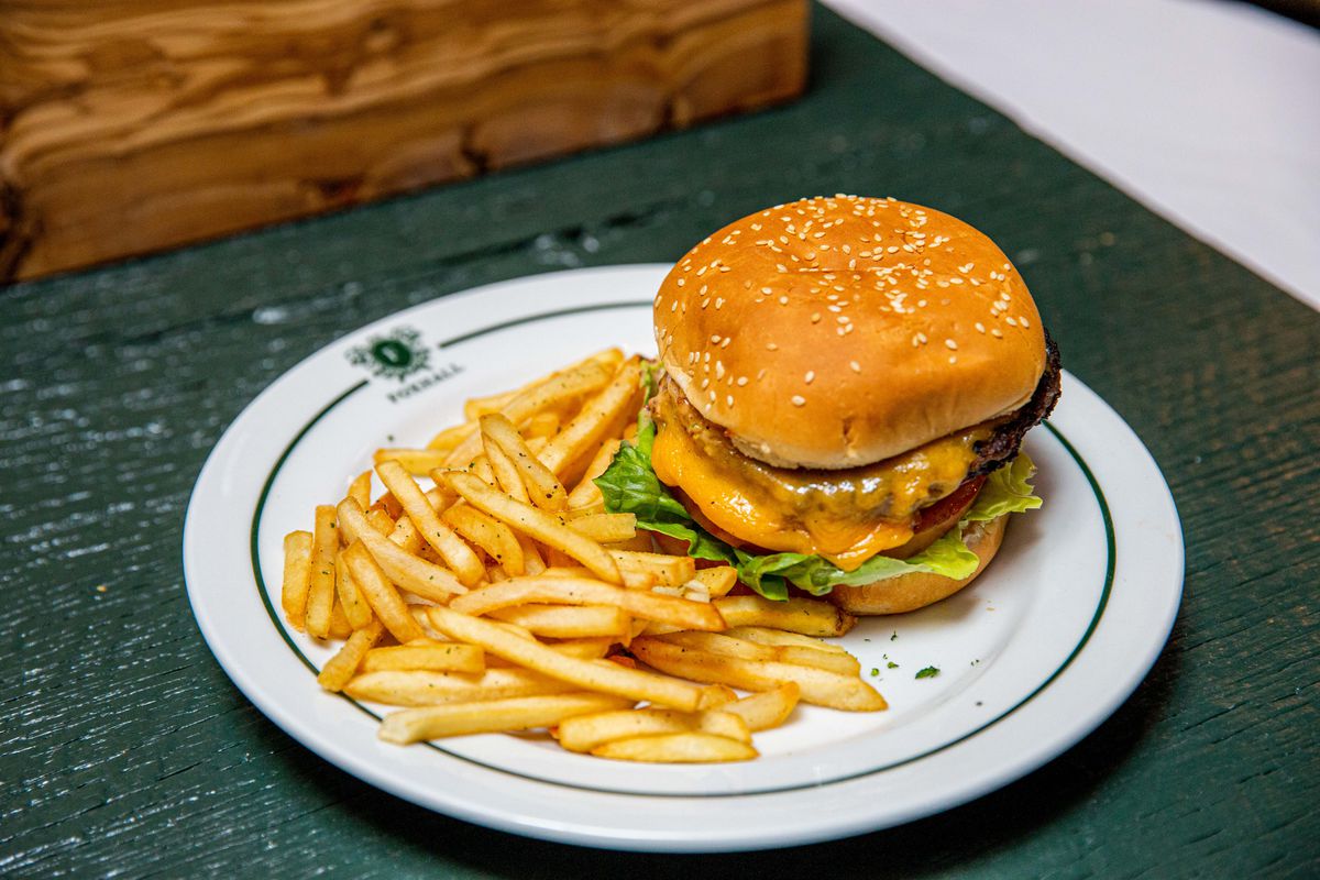 Cheesy burger and fries on a white plate with a green table at a new restaurant.