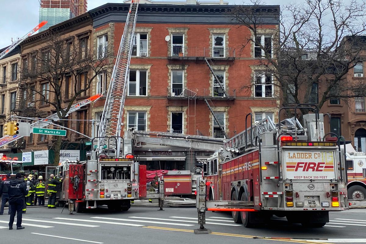 A gutted New York City apartment is surrounded by fire trucks with ladders leaned against the top of the building