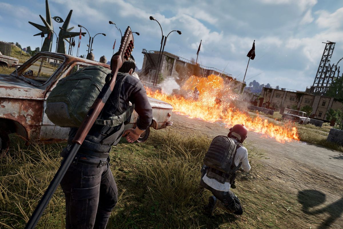 Players crouch behind a rusted-out car while a Molotov cocktail lands in the distance in PUBG