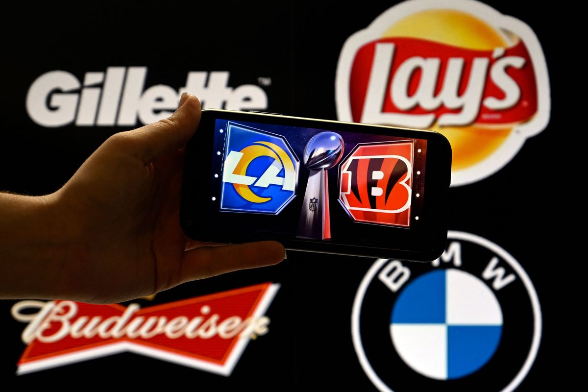 This illustration photo shows the logos of the Cincinnati Bengals and the Los Angeles Rams on a phone in front of the Gillette, Lays, Budweiser and BMW logos displayed on a screen, in Washington, DC, February 9, 2022. -