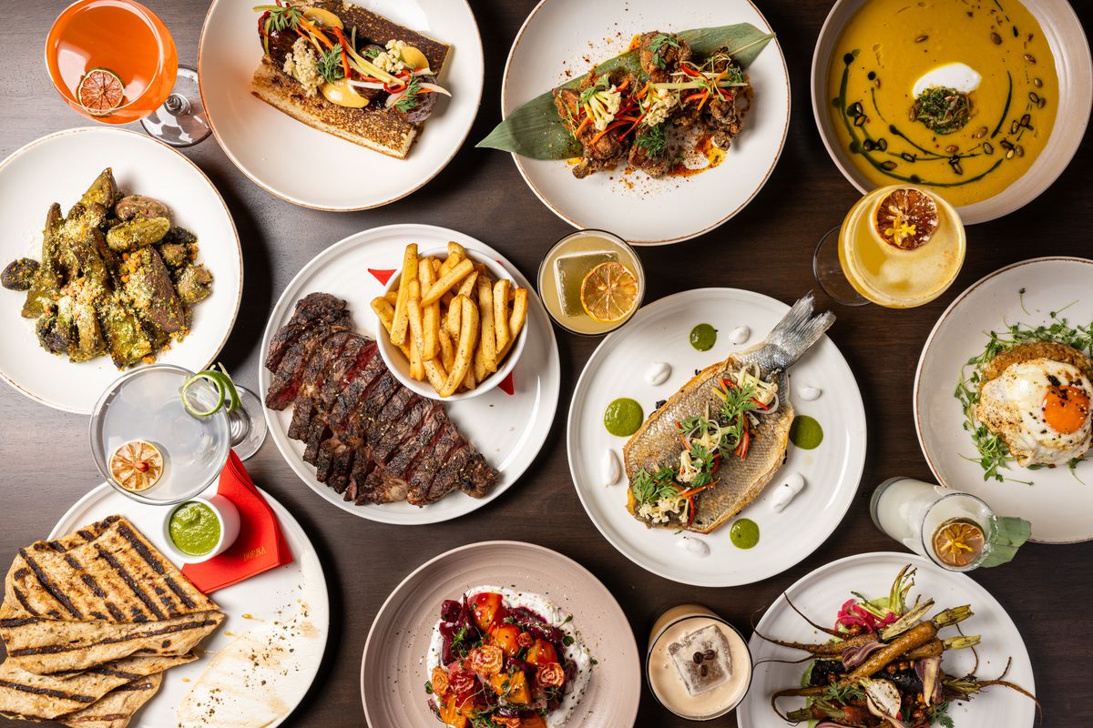 Cut steak, grilled fish, and other California seasonal dishes overlaid on a table.
