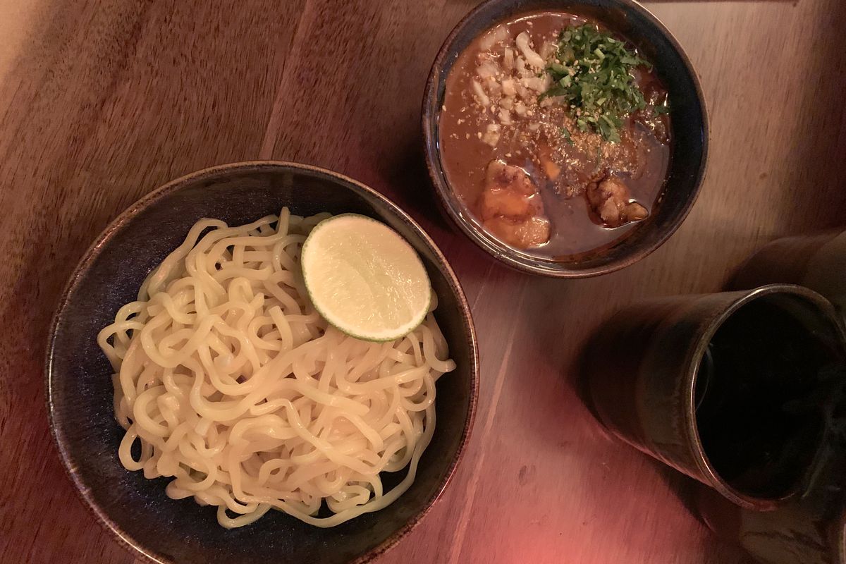 A bowl of noodles next to a bowl of brown soup.