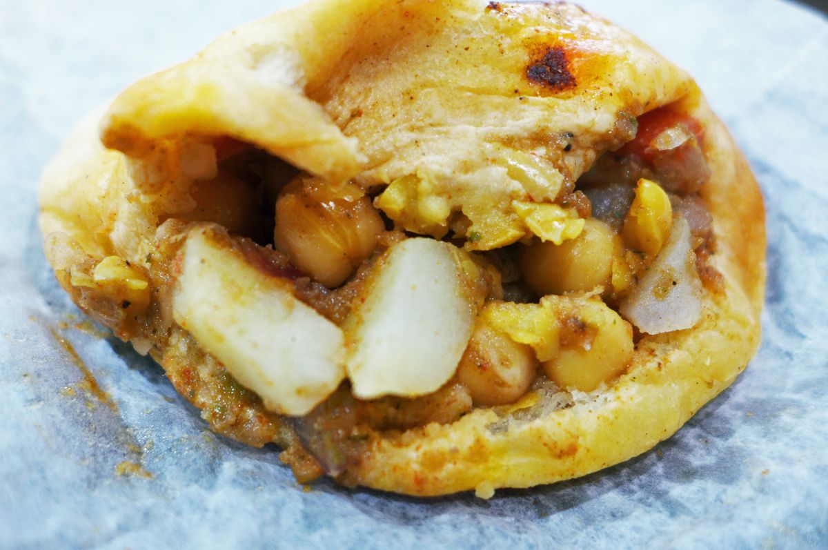 A misshapen roll with chickpeas and potatoes tumbling out.
