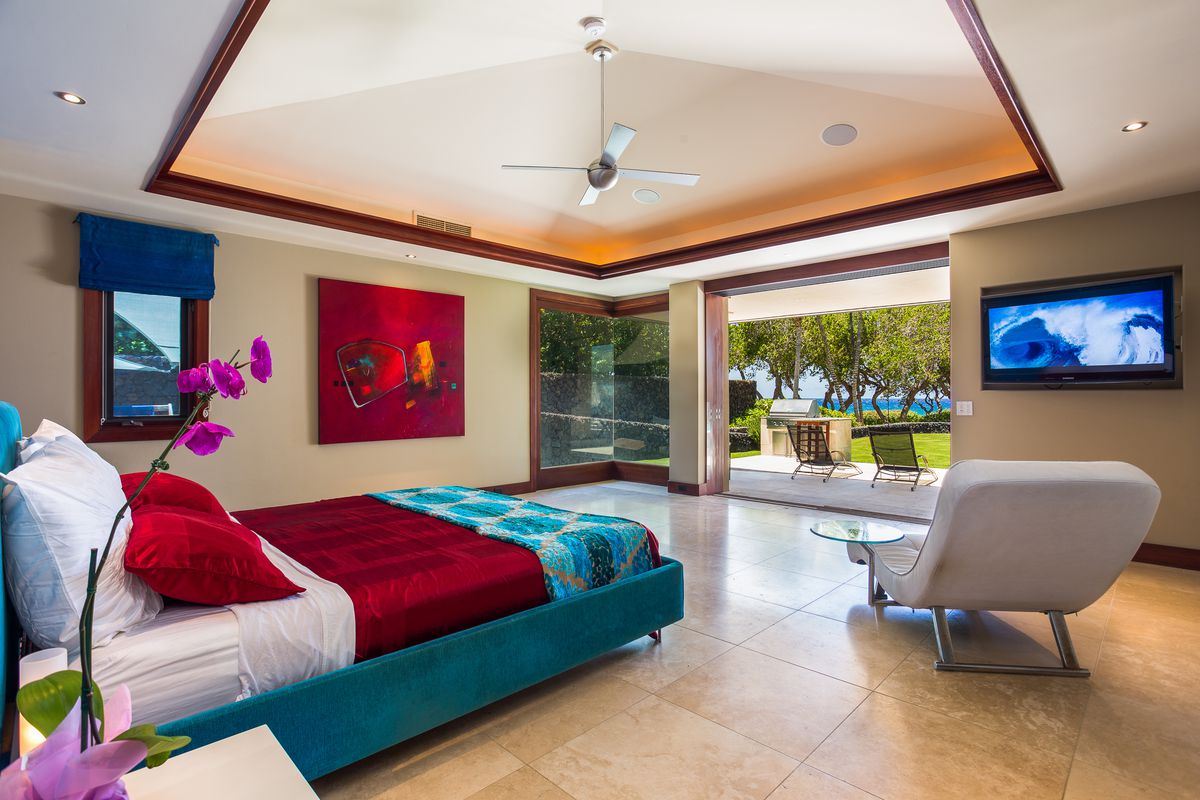A bedroom has polished flors, a red and teal bed, and doors that open to the yard. 