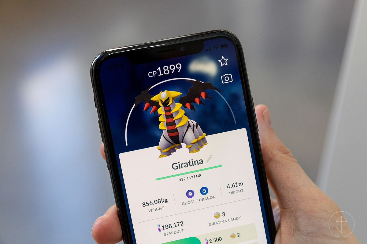 A hand holds up an iPhone displaying Altered Forme Giratina’s stat screen in Pokémon Go