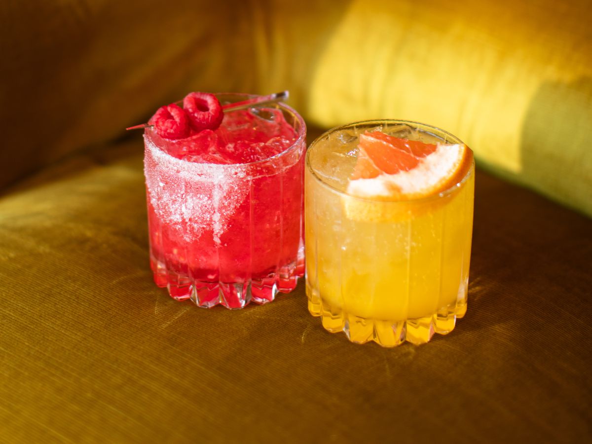 Two cocktails sit on a suede couch.