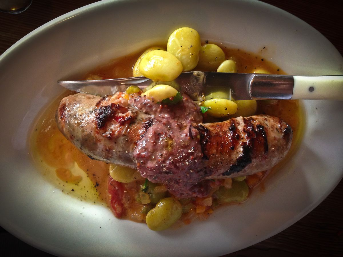 A knife cuts into a whole sausage on a bed of beans, served at Gjelina in Los Angeles.