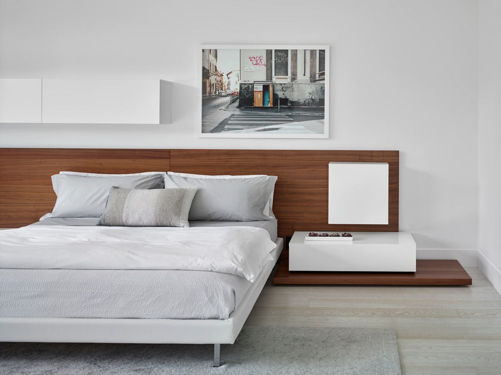 Sleek bed in white walled bedroom with wooden headboard.