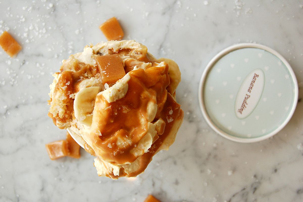 Overhead view of a big scoop of salted caramel banana pudding in a paper cup on a white marble surface.