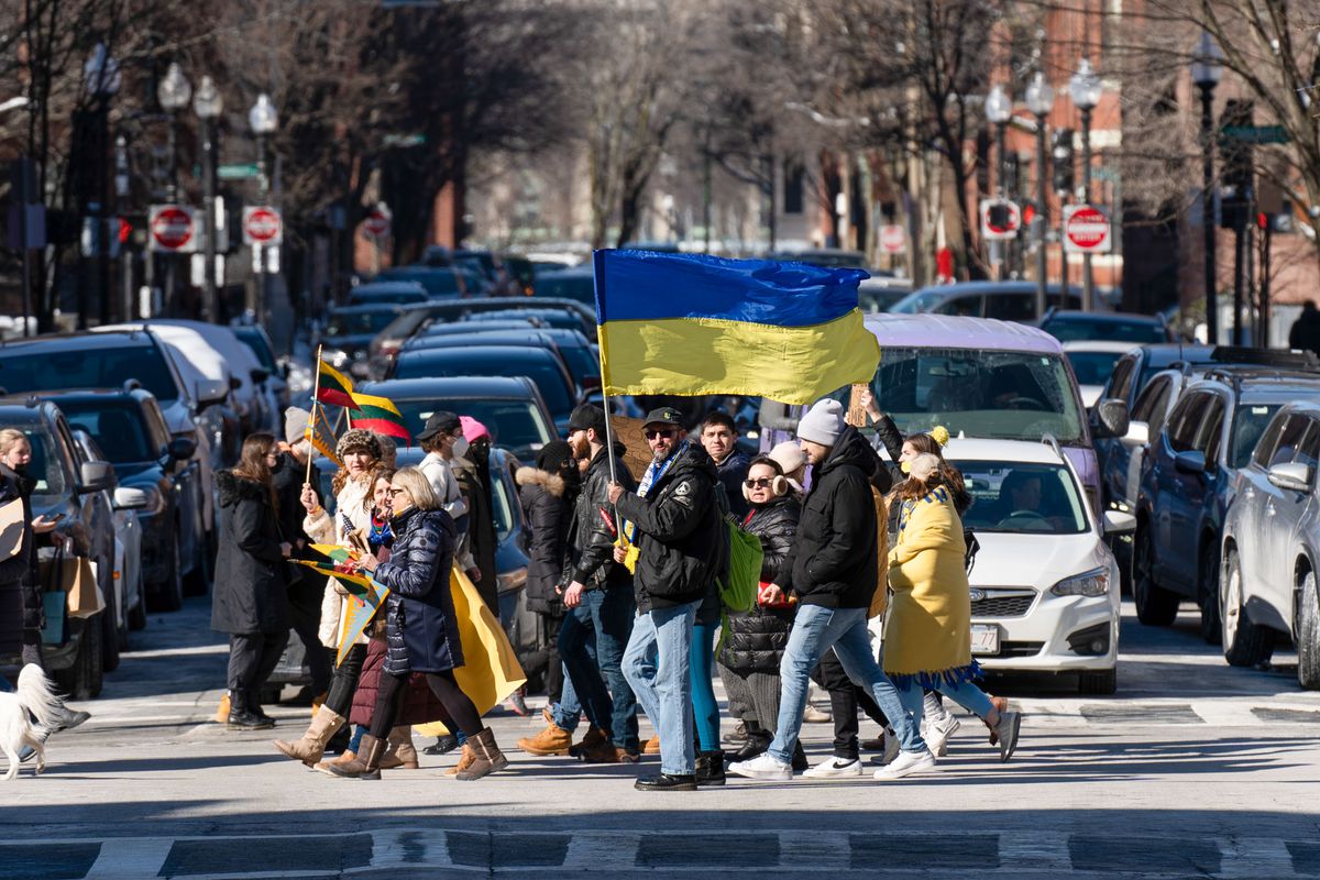 A group of people cross a city street holding a blue and yellow Ukrainian flag.