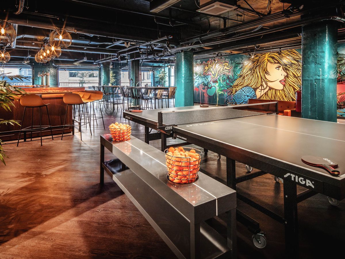 Interior shot of an empty venue with a ping-pong table, bar, and colorful mural that features a woman with long blonde hair and sunglasses.