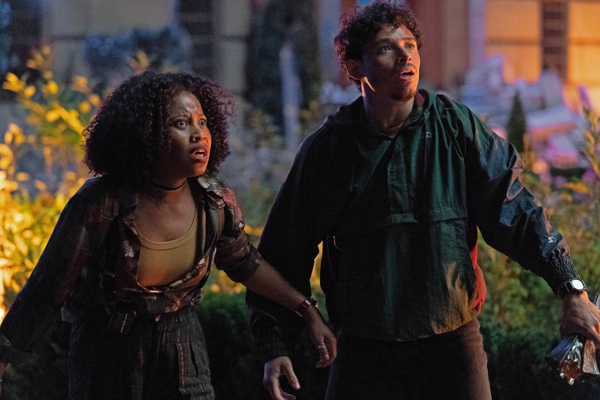 Dominique Fishback and Anthony Ramos stand in a city at night and gape in horror at something offscreen in Transformers: Rise of the Beasts