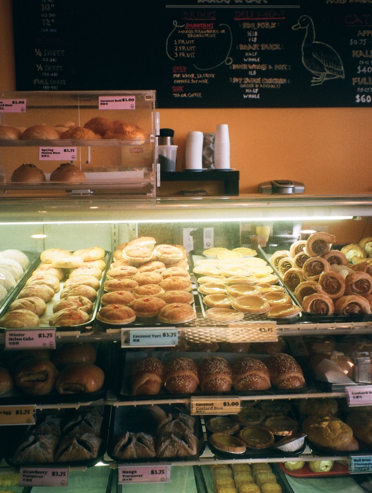 A pastry case full of Chinese pastries, with an orange wall and chalkboard in the background.