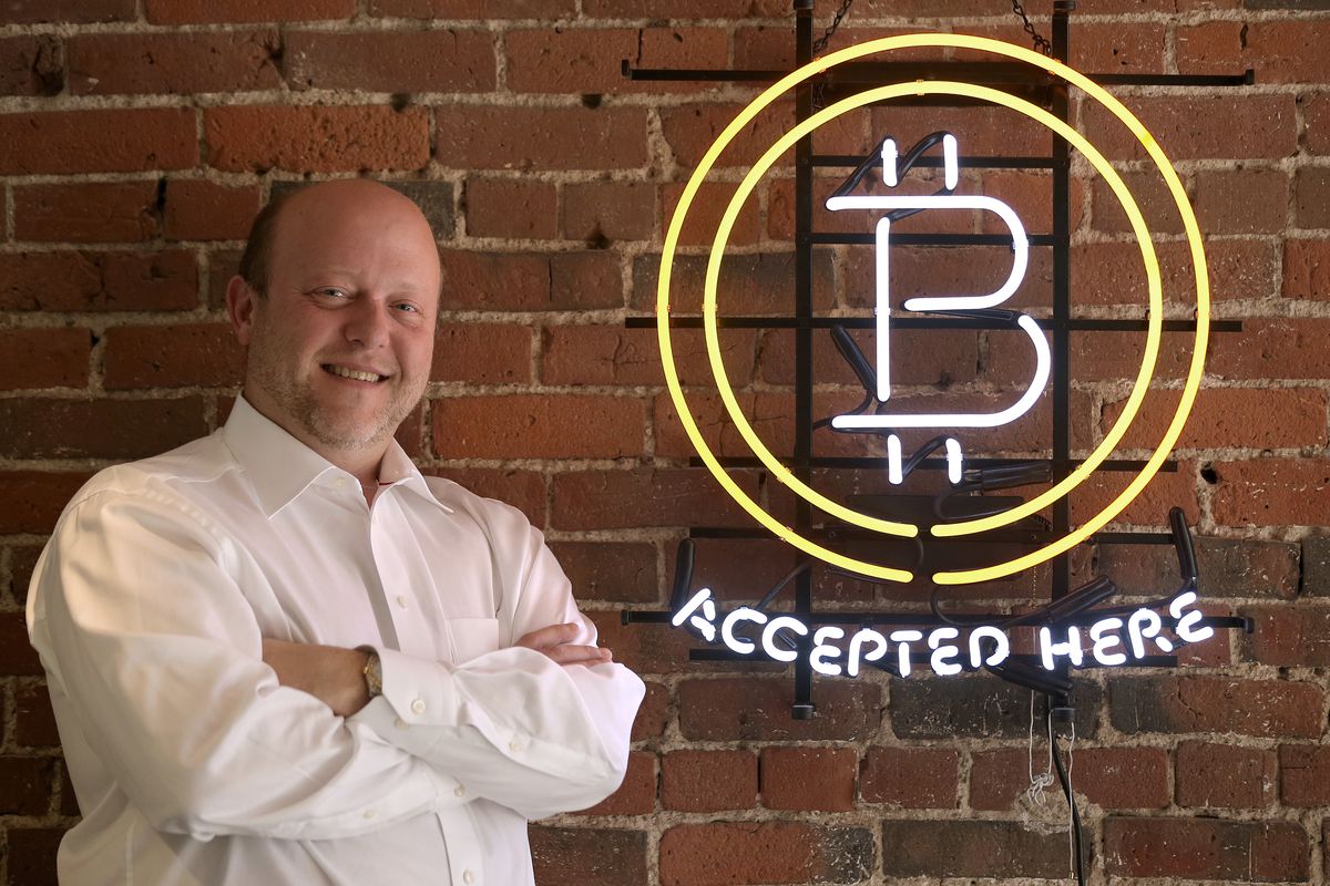 Circle CEO Jeremy Allaire stands next to a neon sign that reads “bitcoin accepted here.”