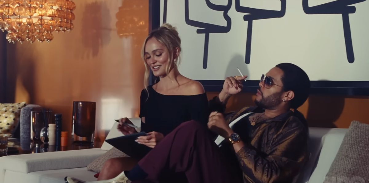 The Weeknd smokes a cigarette while sitting next to Lily-Rose Depp on a couch in The Idol.