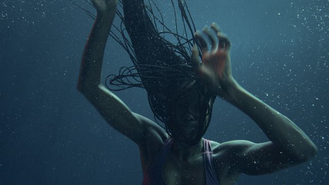 Aisha (Anna Diop), a dark-skinned woman with long, braided hair, is seen in shadow underwater with her hands raised as if she’s descending in Nanny