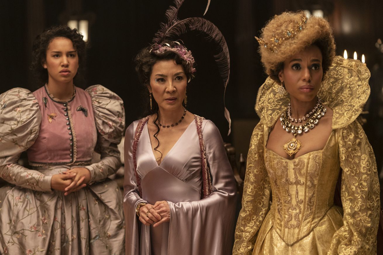 Three women in extravagant, intricate gowns looking to their right in concern at something just off-screen.