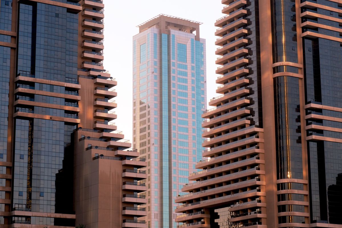 Photo of a skyscraper in the background flanked by two buildings on either side in the foreground. 