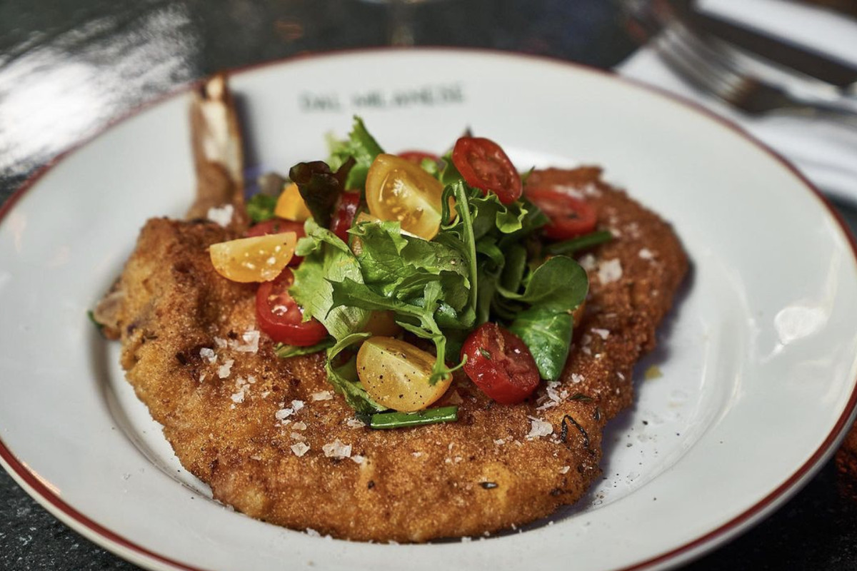 A pounded and breaded veal chop with tomatoes from a restaurant, on a white plate.