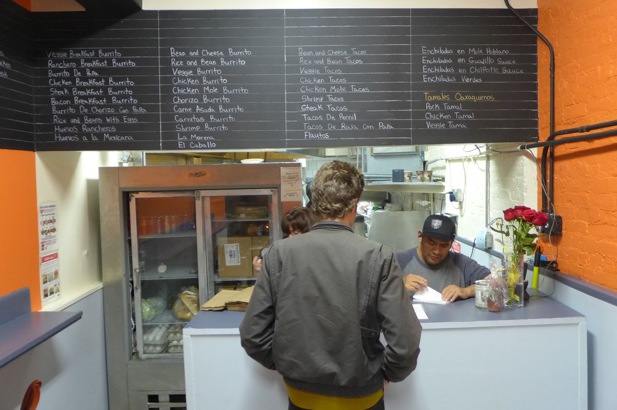 Orange walls, gray trim, and a guy stands before the counter as one of the brothers takes an order.