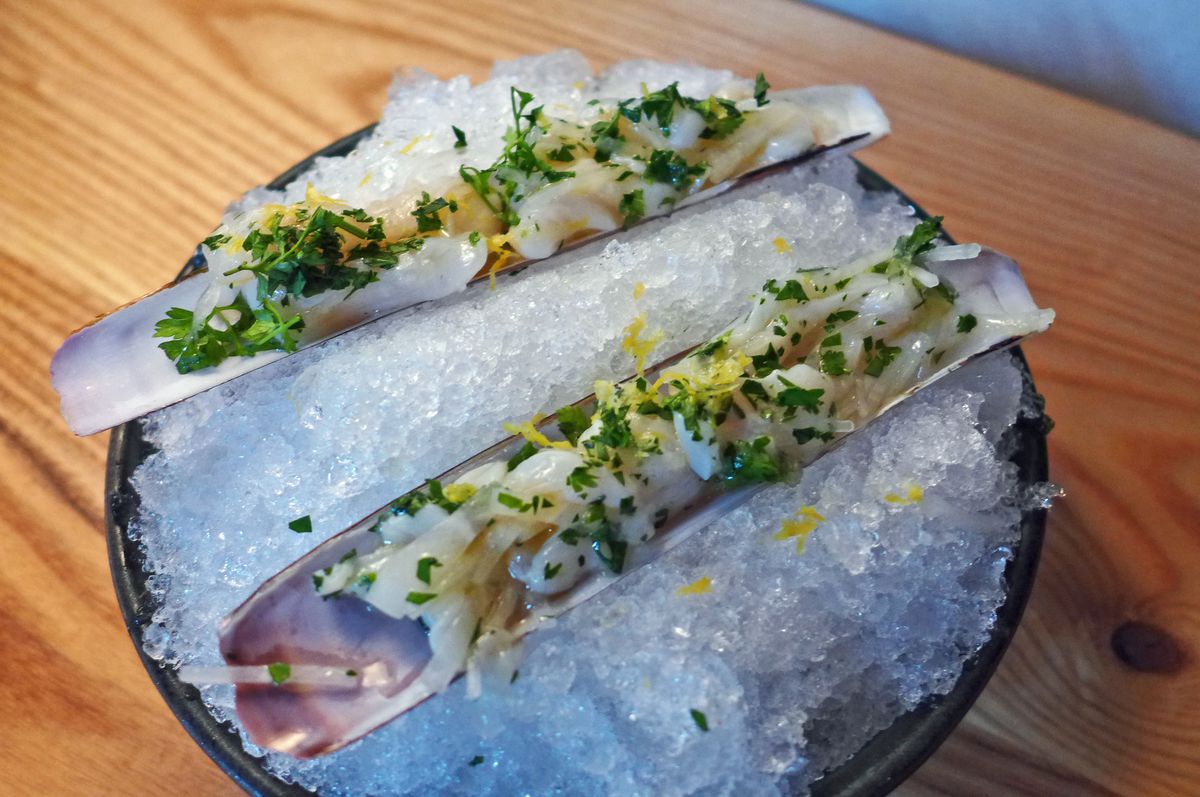 Two long rectangular shells with raw seafood sprinkled with herbs.