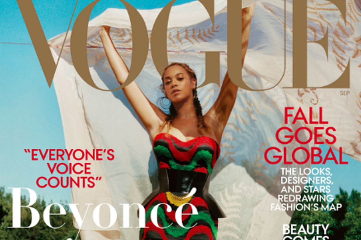 Beyoncé poses in the grass, with woods behind her, wearing a multicolored dress.
