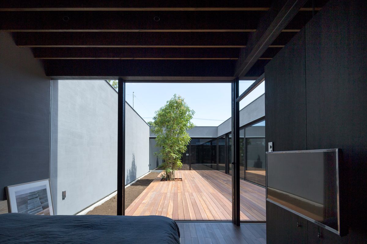 A bedroom looking out onto the courtyard and the living spaces behind glass walls on the other side. 