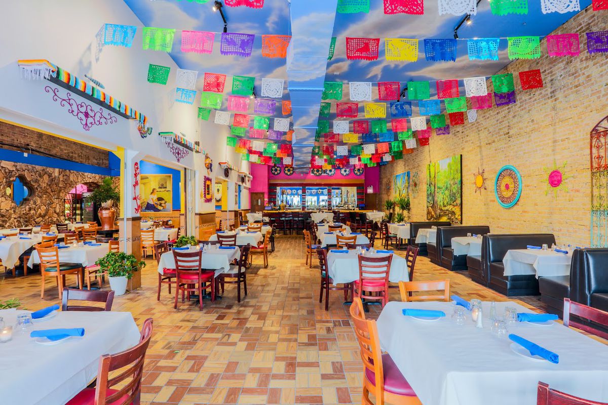 A large, long restaurant dining room decorated with colorful Mexican streamers.