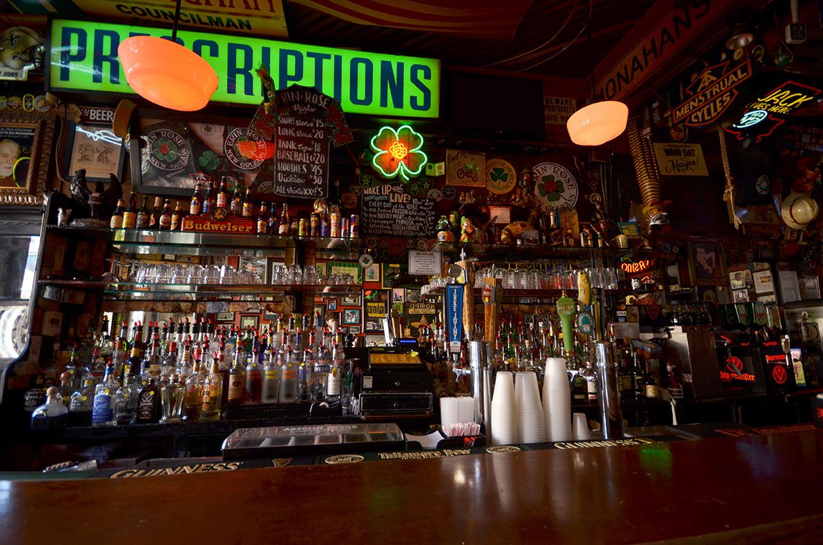 A view of the bar inside Erin Rose with bottles and a green lit up “prescription” sign hanging.