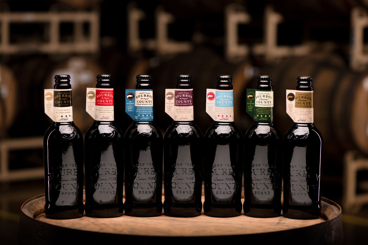 Seven dark beer bottles in a barrel room.