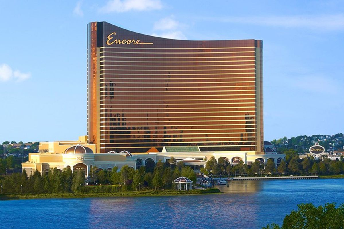 Exterior view of the Encore casino near Boston, a shiny bronze-colored building on a river.