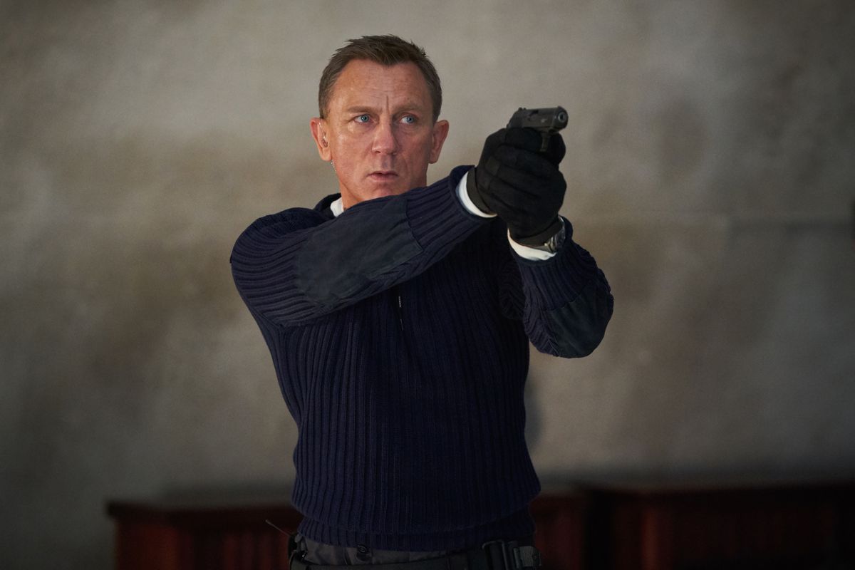 james bond holds his pistol while wearing a blue sweater