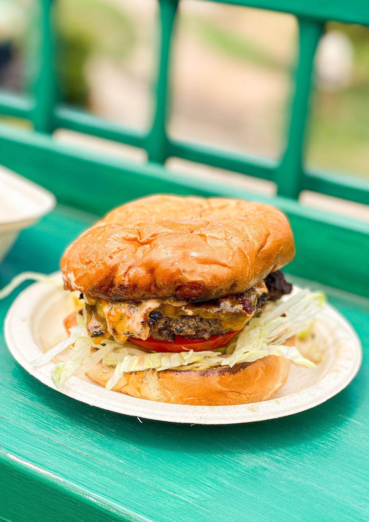 Un hamburger de style arrière-cour avec des bords sombres et des légumes sur un petit pain bronzé, montré de près.